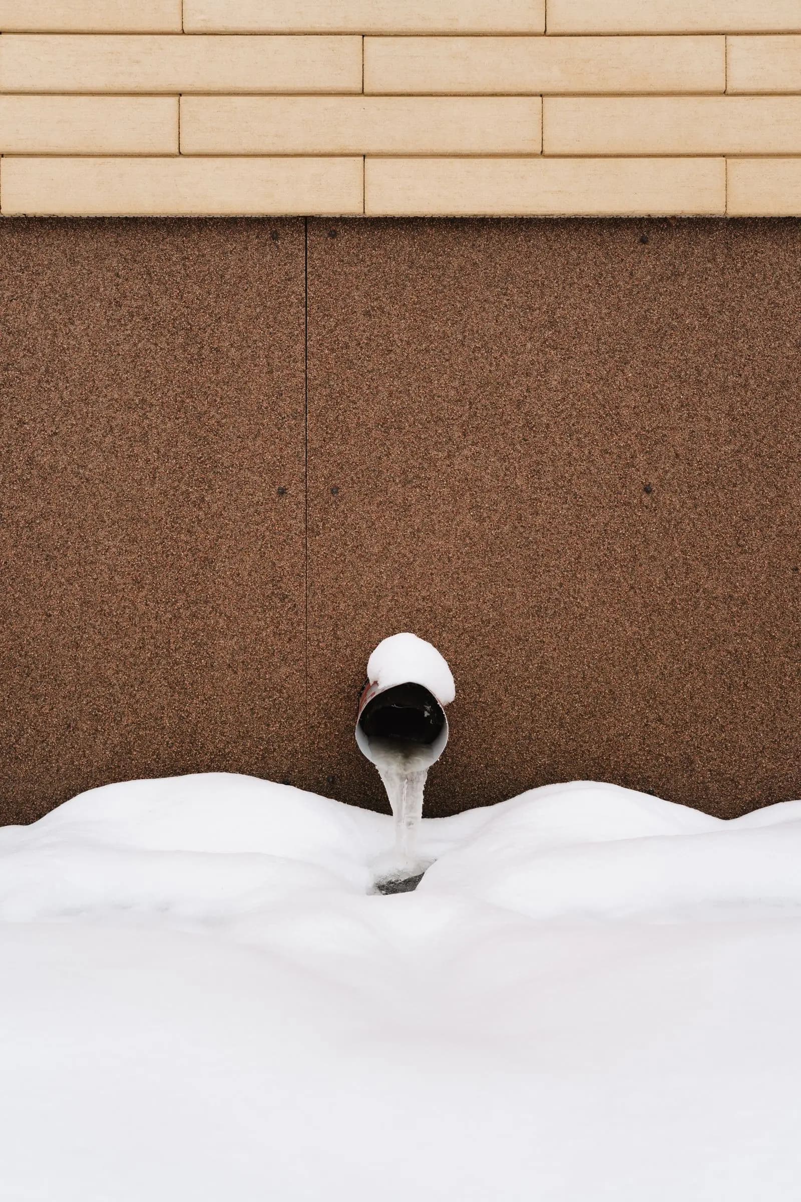 Frozen pipe covered in snow against a building wall